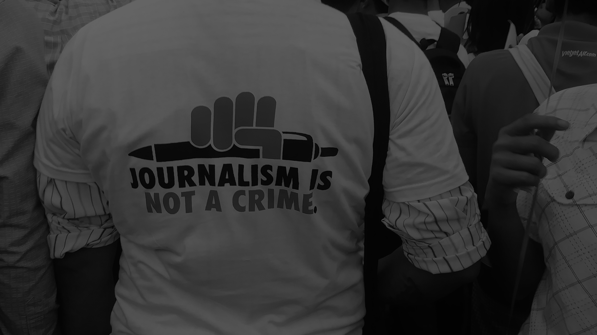 The back of a person in a crowd with a shirt that says Journalism is not a crime.
